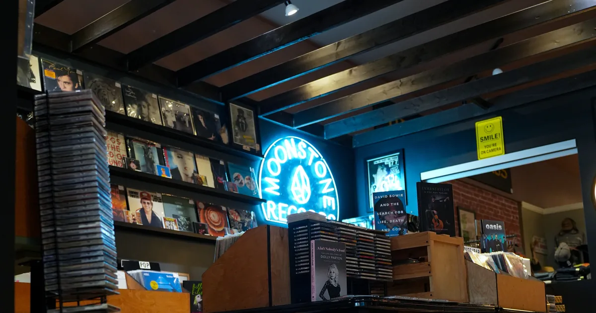The inside of Moonstone Records, walls lined with album covers and a neon sign glowing blue over the record bins.
